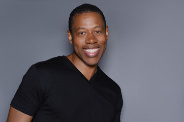 Portrait of  smiling African American man in plain black t-shirt standing in front of gray background