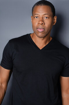 Portrait of  African American man in plain black t-shirt standing in front of gray background