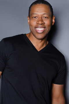 Portrait of  smiling African American man in plain black t-shirt standing in front of gray background