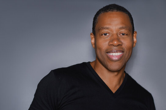 Portrait of  smiling African American man in plain black t-shirt standing in front of gray background