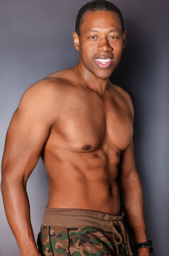 Portrait of shirtless, athletic Black man standing in front of gray wall