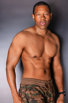 Portrait of shirtless, athletic Black man standing in front of gray wall
