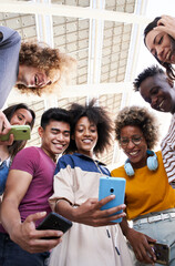 Vertical photo. Low angle view of a group of young teenagers holding cell phones. Concept of...