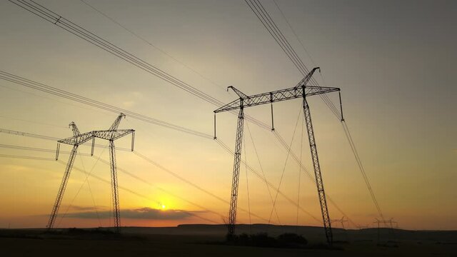 Dark silhouette of high voltage towers with electric power lines at sunrise.