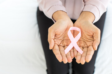 Pink ribbon, on aged hand of illness woman, representing international fabric symbol of breast...