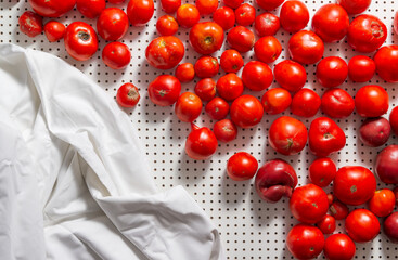 Red tomatoes are scattered on a white board, next to the fabric with folds lies.