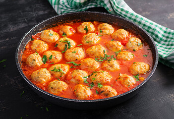 Meatballs in tomato sauce in a frying pan on dark background.