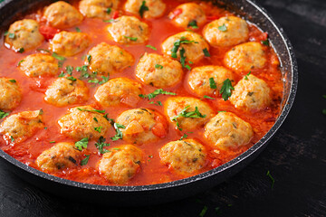 Meatballs in tomato sauce in a frying pan on dark background.