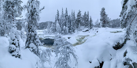Panorama of an ice-covered river with waterfall in frozen taiga spruce forest