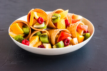 a white plate with waffle cones filled with fruit on a black background.