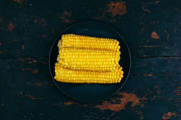 ears of boiled corn on a black plate on a wooden vintage black grunge background top view