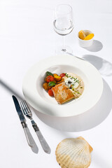 Fish steak with fillet tuna, warm tomato, baked potato and vitello tonnato sauce. Fish in white plate. Tuna sauce and vegetables. Contemporary seafood restaurant menu, summer day with sunlight shadow.