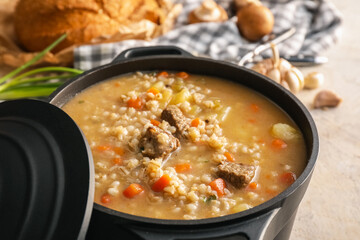 Cooking pot with tasty beef barley soup on grunge background