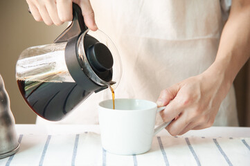 Fototapeta na wymiar Crop of barista pouring black coffee in white and empty cup at home