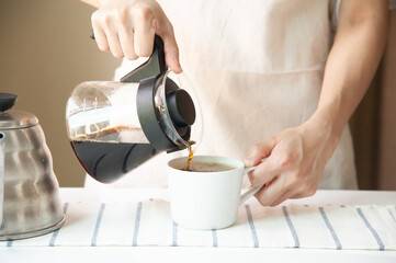 Barista pouring black coffee in white and full cup at home