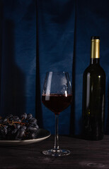A bottle of red wine, a glass and grapes on a dark background.