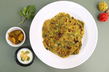 A Food called Methi paratha or Methi thepla is an Indian breakfast dish served with curd boondi raita and capsicum sabzi. Masala Fenugreek roti with copy space.
