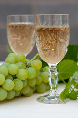 Two glasses of white wine, bunches of grapes and a young vine on a light wooden background. A vertical snapshot.