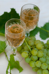 Two glasses of white wine, bunches of grapes and a young vine on a light wooden background. A vertical snapshot.