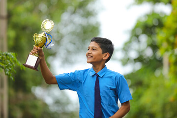 Clever schoolboy raising his trophy as a winner in school competition.