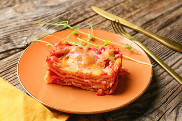 Plate with piece of tasty tomato lasagna on wooden background