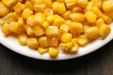 Plate with corn kernels on wooden background, closeup