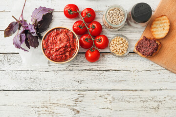 Bowl of tasty pesto sauce, ingredients and toasts on light wooden background