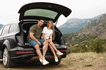 Fototapeta na wymiar Young happy couple on a road trip sitting in car trunk