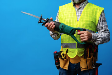 Handyman in uniform holding saw against blue background