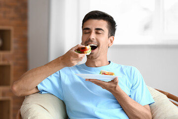 Young man eating tasty sandwich at home