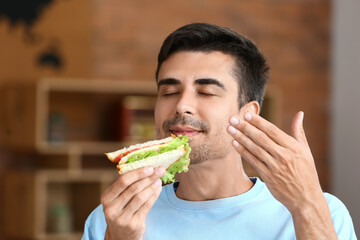 Young man eating tasty sandwich at home