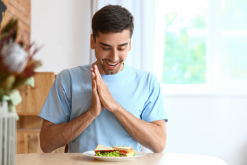 Young man with tasty sandwich at home