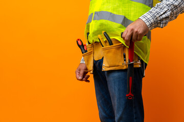 Studio shot of unknown handyman with hands on waist and tool belt with construction tools