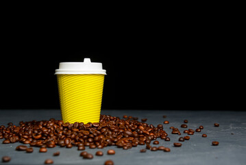 Closed take-out coffee with cup holder. One yellow cup with coffee beans over black background.