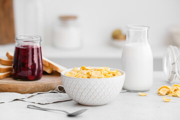 Bowl with tasty corn flakes, bottle of milk and jam on table in kitchen