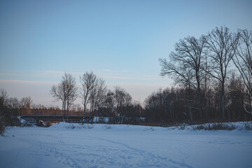 golden winter evening landscape from frozen snow and ice covered river, dry yellow reeds in distance, clear sky, copy space, footprints in snow, transport bridge further. Latvia landscape in cold