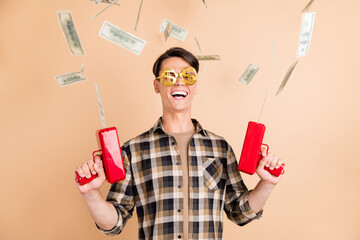 Photo of cheerful crazy guy hold pistol throw blow money wear specs plaid shirt isolated beige...