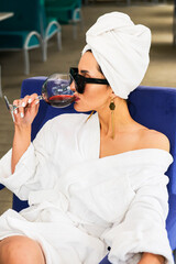 Young caucasian girl in a bathrobe and a towel relaxing with a glass of wine.