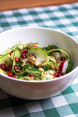 A large dish with a grilled zucchini salad with fresh cucumbers, radish, pomegranate seeds and fresh arugula.