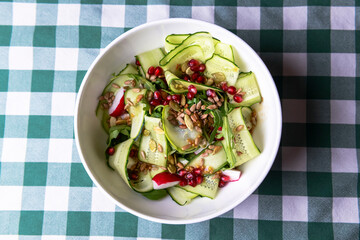 A large dish with a grilled zucchini salad with fresh cucumbers, radish, pomegranate seeds and fresh arugula.