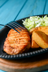 Grilled Chicken Steak with fried potatoes in rural style and coleslaw salad served in a tray over blue background.