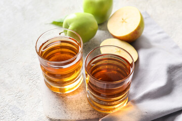 Glasses of apple juice and fresh fruits on light background