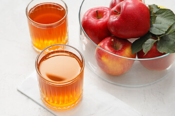 Glasses of apple juice and fresh fruits on light background