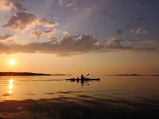 Fototapeta na wymiar Kayaking silhouette on a calm sea far away at sunset.