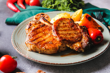 Plate with tasty pork steaks and grilled vegetables on table