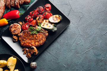 Plate with tasty pork steak and vegetables on dark background