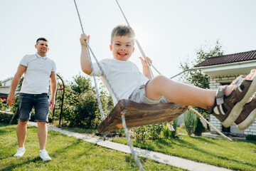 A boy with Down syndrome having fun on a swing with his father. Everyday life of a disabled child....