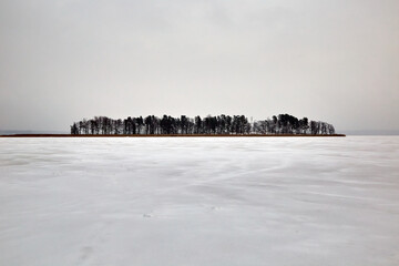 Small island in a frozen lake in snowy winter