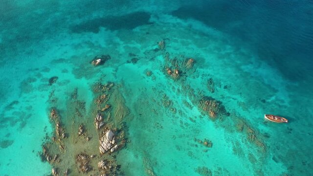 View from above, stunning aerial view of a wooden boat anchored to some rocks bathed by a crystal clear, turquoise water. Giardinelli island, La Maddalena Archipelago, Sardinia, Italy.