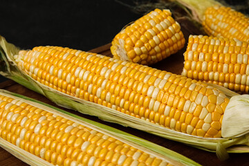 Wooden board with fresh corn cobs, closeup